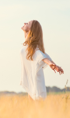 A picture of a woman standing in the field and feeling the wind with her arms outstretched.