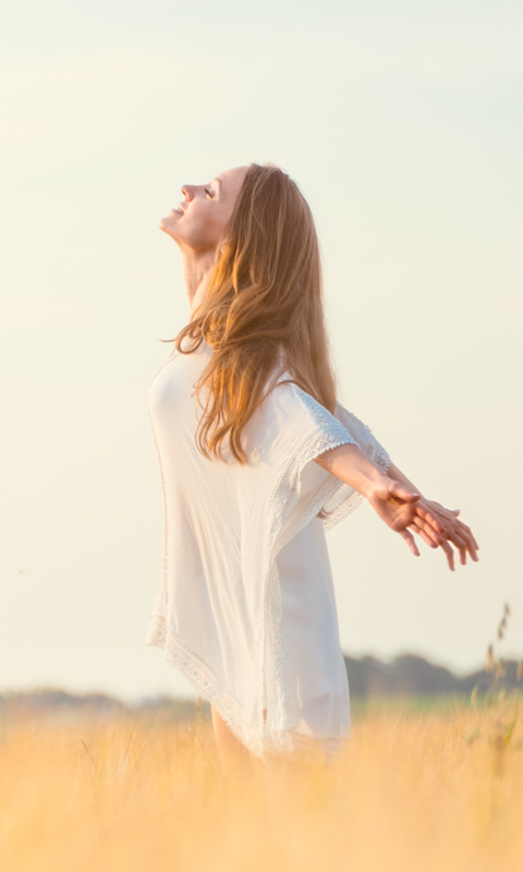 A picture of a woman standing in the field and feeling the wind with her arms outstretched.